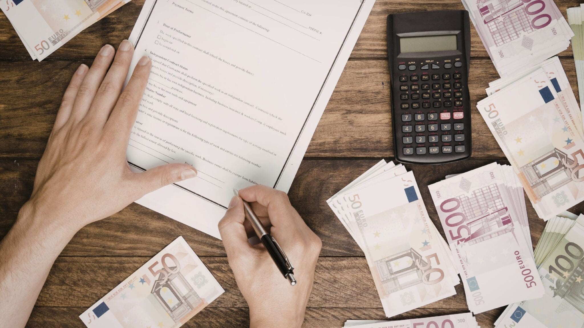 Person filling out a financial form with money and calculator nearby.